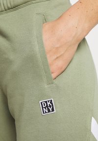Gröna bomullsmjukisbyxor med en ficka, prydda med en DKNY-logotyp i svart och vitt. Slät textur och avslappnad passform.