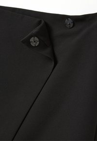 Gros plan sur un tissu noir avec deux fermoirs à pression ronds noirs, l'un ouvert et l'autre fermé, sur des bords se chevauchant.