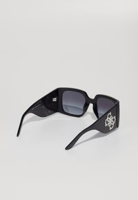 Gafas de sol negras con montura rectangular, lentes degradados y brazos negros texturizados que presentan un destacado detalle del logo en plata.