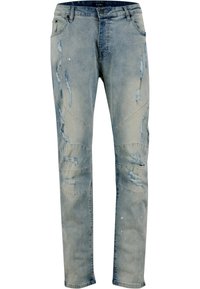 Vaqueros de denim azul claro con parches desgastados, áreas descoloridas y sutiles salpicaduras de pintura blanca. Diseño clásico de cinco bolsillos y ajuste slim.