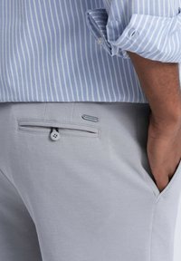 Hellgraue Hose mit strukturiertem Finish, ausgestattet mit einer Gesäßtasche mit Knopfverschluss und einem dekorativen Hardware-Akzent.