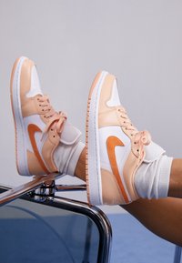 Baskets montantes au design rose et blanc, avec un swoosh orange, un cuir texturé et une semelle en caoutchouc.