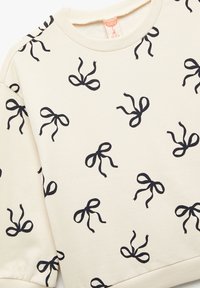 Creme sweatshirt med sort sløjfeprint. Blødt materiale med rund halsudskæring og ribbede manchetter. Casual design, velegnet til lag-på-lag.