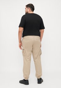 Beżowe spodnie cargo z elastycznymi mankietami, bocznymi kieszeniami i tylnymi kieszeniami, w połączeniu z czarnym t-shirtem z krótkim rękawem. Prosty design i materiał bawełniany.