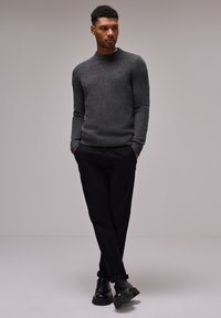 Pull en tricot gris avec col rond, poignets et ourlet côtelés ; associé à un pantalon noir et des chaussures noires, créant une tenue monochrome.