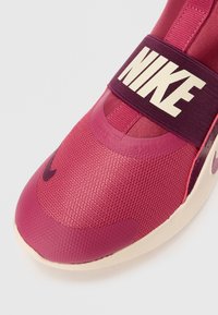 Lähikuvassa punainen Nike sneaker, mille on iseloomulik võrgumaterjalist ülemine osa, tekstuuriga varbakaitse ja tumepruun rihm, millel on julge valge Nike logo.