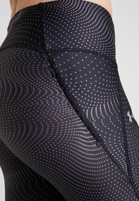 Leggings atletici neri con un motivo testurizzato di punti grigi chiari e linee ondulate. Le caratteristiche includono una tasca con zip e un design aderente.
