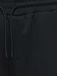 Taille élastique noire avec cordon noir et vue partielle d'une poche sur un pantalon en tissu noir.