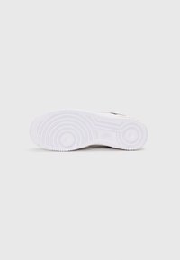 Sola de sapatilha com exterior de borracha branca; apresenta padrões circulares e ranhuras para tração; design minimalista sem marcas visíveis.