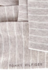 Ljust grå strumpor med subtila vertikala ränder, texturerad tyg och en tryckt logotyp "TOMMY HILFIGER" nära skaftet.