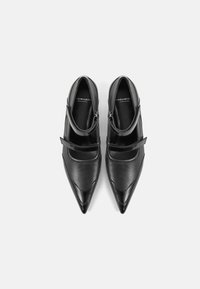 Chaussures en cuir noir avec un bout pointu, dotées de deux brides réglables au niveau du cou-de-pied et d'une texture lisse.
