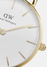 Goldfarbene Armbanduhr mit weißem Zifferblatt. Verfügt über minimalistische Stundenmarkierungen, schlanke Zeiger und eine strukturierte Krone. Stilvolles und raffiniertes Design.