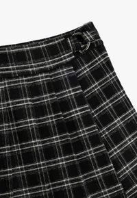 Gonna a quadri bianca e nera con una trama testurizzata. Presenta un dettaglio a fibbia in vita e un design plissettato in tutta la lunghezza.