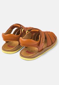 Braune Leder-Kinderschuhe mit gelben Gummisohlen, verstellbaren Klettverschlüssen und offenem Fersen- und Zehendesign.