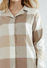 Button-up shirt in beige and cream check pattern, featuring a collar, long sleeves, and smooth fabric texture.