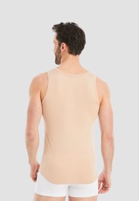 Beige tank top with a rounded neckline and straight hem, made from soft fabric. Worn over white shorts, showing a fitted style.