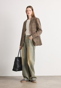 Blazer à carreaux marron et beige, pull crème, jean large délavé, baskets grises et sac à main noir en cuir tressé. Textures douces et coupe décontractée.