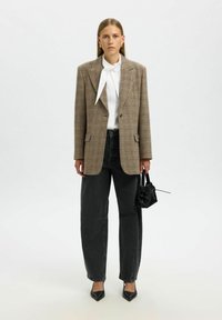 Blazer oversize à carreaux marron, chemise blanche avec cravate, jeans noirs taille haute droits, talons aiguilles noirs et un petit sac noir.