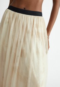 Una gonna in tulle beige con una vita elastica nera che presenta il nome del brand "LIU-JO". Il tessuto ha una leggera lucentezza e una texture a strati.