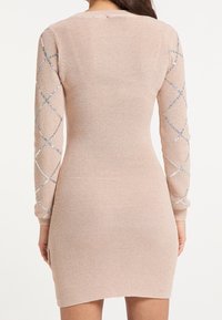 Abito a maglia di un rosa chiaro con maniche lunghe, caratterizzato da motivi a forma di diamante in paillettes sulle braccia. Design aderente con scollo rotondo.