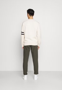 Krämfärgad tröja med svarta ränder på ärmen, kombinerad med olivgröna byxor. Vita sneakers fulländar outfiten.