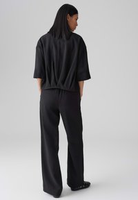 Maglia nera oversize con maniche corte e vestibilità ampia, abbinata a pantaloni neri a gamba larga. Tessuto liscio e silhouette casual.