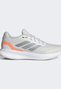 Helle graue Sportschuhe mit einer strukturierten Oberseite, orangefarbenen Akzenten, silbernen Streifen und einer geriffelten weißen Gummisohle, die mit "CLOUDFOAM" gekennzeichnet ist.