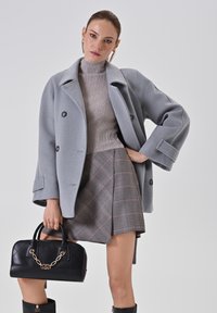 Cappotto grigio doppiopetto, maglione grigio a coste, gonna a quadri grigia e bordeaux, borsa nera trapuntata con catena dorata, stivali neri al ginocchio.