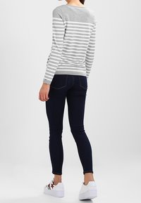 Maglione grigio a righe con maniche lunghe, abbinato a jeans skinny blu scuro e sneakers bianche con dettagli di stelle rosse.
