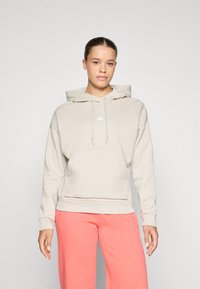 Hooded sweatshirt, licht beige, zachte stof, kangoeroezak, verstelbare koord, wit logo-detail, gecombineerd met roze joggingbroek.
