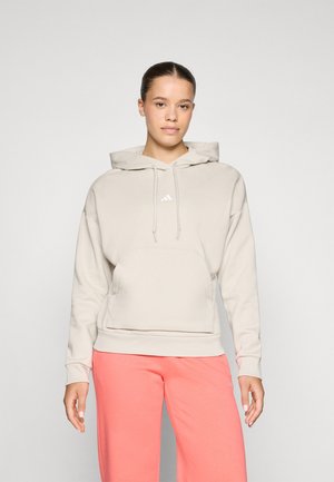 Hooded sweatshirt, light beige, soft fabric, kangaroo pocket, adjustable drawstring, white logo detail, paired with pink sweatpants.