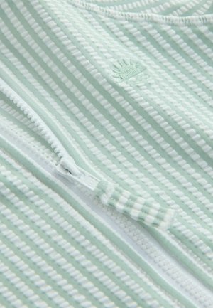 Țesătură cu dungi verzi deschise și accente albe, prevăzută cu un fermoar și un logo în formă de scoică în relief. Textură netedă și detalii cu model zimțat.