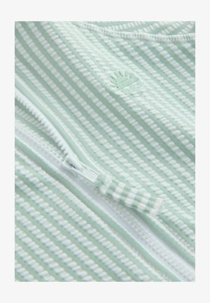 Šviesiai žalia dryžuota medžiaga su baltais akcentais, su užtrauktuku ir įspaustu kriauklės logotipu. Lygios tekstūros ir su riboto rašto detalėmis.