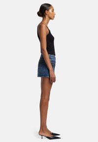 Top nero con spalline sottili, mini gonna di jeans con decorazioni argentate e sabot neri con tacco a punta, mostrati di lato.