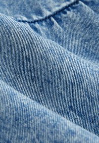 Denim tkanina u svijetloplavoj boji s izraženom teksturom i suptilnim sjenčanjima, koja prikazuje čvrsto tkanu nit i blage varijacije u boji.