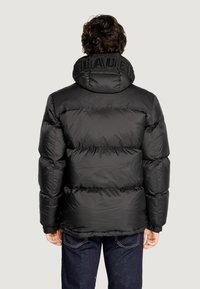 Giacca a vento nera con design trapuntato, colletto alto e nome del marchio impresso sul collo. Presenta polsini elasticizzati e una texture liscia e lucida.