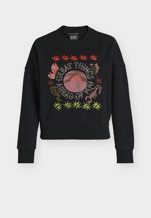 Μαύρο φούτερ με πολύχρωμα κεντημένα αστέρια, φύλλα φυτών, έναν σκορπιό και το κείμενο «Μεγάλα πράγματα σε περιμένουν» γύρω από ένα ροζ σχέδιο ήλιου και λόφου.