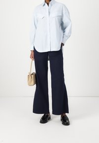 Ljusblå randig skjorta med knappar och spetsig krage, två bröstfickor. Breda marinblå byxor och svarta skor. Beigefärgad handväska.