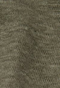 Strikket stof i olivengrøn, med en glat tekstur og et ensartet mønster med subtile variationer i maskerens tykkelse.