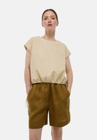Haut beige à manches courtes avec une taille élastique, associé à un short marron avec poches latérales et liens ajustables. Design simple et décontracté.