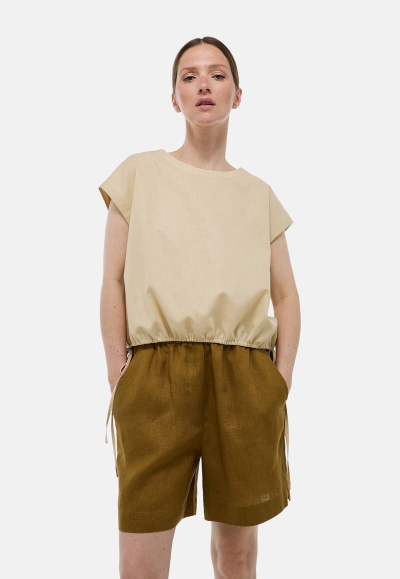 Haut beige à manches courtes avec une taille élastique, associé à un short marron avec poches latérales et liens ajustables. Design simple et décontracté.