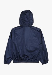 Giacca blu navy con cappuccio, polsini ed elastico in vita. Materiale liscio e lucido con dettagli minimi e una forma rilassata e oversize.