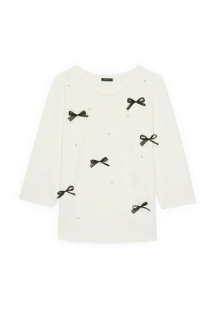 Valkoinen pitkähihainen paita pyöreällä kaula-aukolla, koristeltu kuudella mustalla pienellä rusetilla ja hajanaisilla pienillä helmimäisillä helmillä.