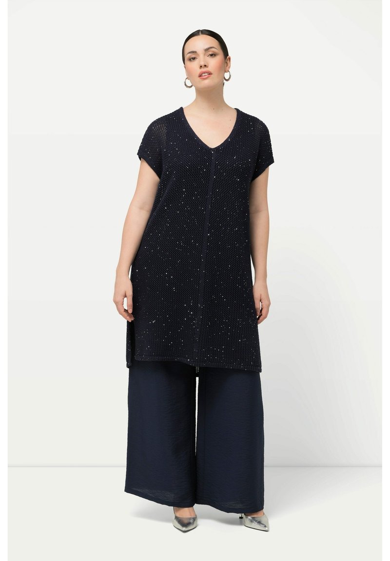 Túnica marina de manga corta, con tejido texturizado y adornos plateados. Combinada con pantalones de pierna ancha en azul marino y zapatos plateados.