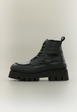 Botte à plateforme épaisse en cuir noir avec laçage à l’avant et semelle épaisse rainurée, vue de côté sur un fond neutre.