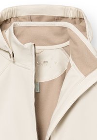 Cremefarbene Jacke mit einem Reißverschluss, ausgestattet mit einem weichen beige Fleece-Futter und subtilen Stickdetails rund um die Kapuze und den Kragen.
