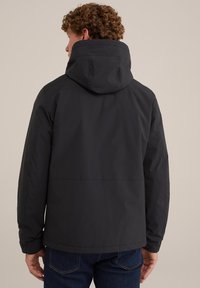 Chaqueta negra con capucha hecha de una tela suave. Presenta un corte ligeramente holgado y costuras visibles, con un dobladillo plano y un diseño minimalista.