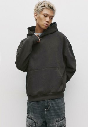Zwarte oversized hoodie van zacht stof, met een kangoeroezak en geribde manchetten. Minimalistisch ontwerp zonder zichtbare logo's of versieringen.