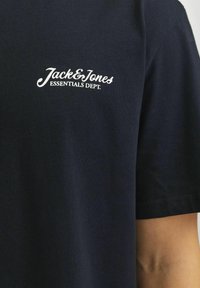 Camiseta de algodón de color azul marino con un logotipo bordado en blanco "Jack&Jones ESSENTIALS DEPT." en el área del pecho izquierdo, de mangas cortas y textura suave.