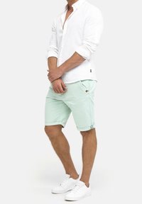 Vit linne skjorta med knappar, mintgröna shorts med uppvikta fållar och vita sneakers. Shortsen har en liten brun accenttag.